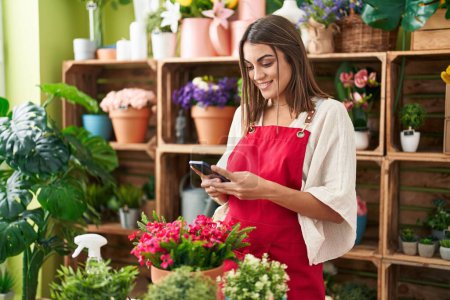 Photo for Young beautiful hispanic woman florist smiling confident using smartphone at flower shop - Royalty Free Image