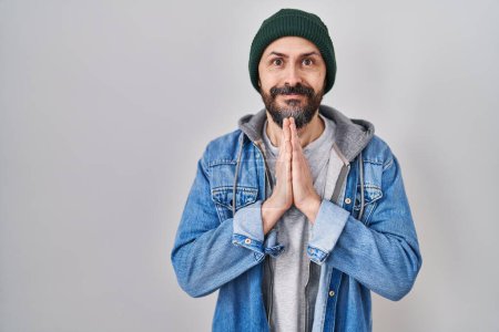Photo for Young hispanic man with tattoos wearing wool cap praying with hands together asking for forgiveness smiling confident. - Royalty Free Image