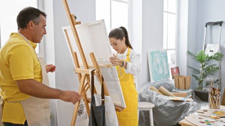 Téléchargez les photos : Artistes hommes et femmes préparant des toiles sur chevalet, commençant leur voyage de peinture ensemble dans un atelier d'art - en image libre de droit