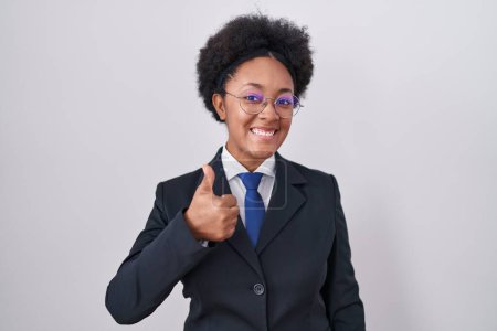 Photo for Beautiful african woman with curly hair wearing business jacket and glasses doing happy thumbs up gesture with hand. approving expression looking at the camera showing success. - Royalty Free Image