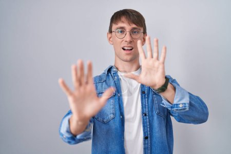 Photo for Caucasian blond man standing wearing glasses afraid and terrified with fear expression stop gesture with hands, shouting in shock. panic concept. - Royalty Free Image