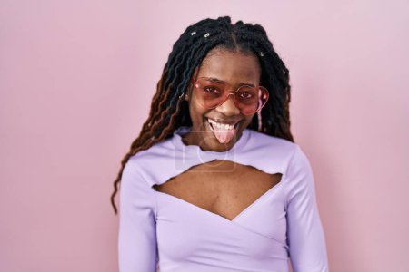Photo for African woman with braided hair standing over pink background sticking tongue out happy with funny expression. emotion concept. - Royalty Free Image