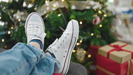 Photo for Young hispanic man lying by christmas tree moving feet at home - Royalty Free Image