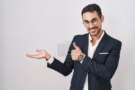 Téléchargez les photos : Beau homme d'affaires hispanique debout sur fond blanc montrant la main de la paume et faisant un geste correct avec les pouces levés, souriant heureux et joyeux - en image libre de droit