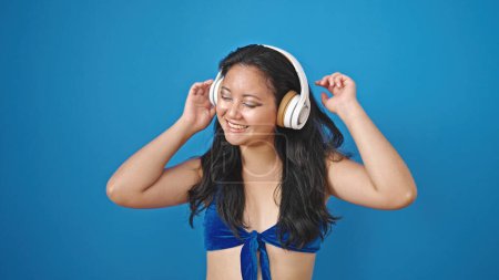 Photo for Young chinese woman tourist wearing bikini listening to music dancing over isolated blue background - Royalty Free Image
