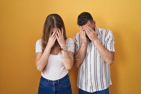 Photo for Young couple standing over yellow background with sad expression covering face with hands while crying. depression concept. - Royalty Free Image