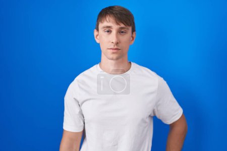 Photo for Caucasian blond man standing over blue background relaxed with serious expression on face. simple and natural looking at the camera. - Royalty Free Image