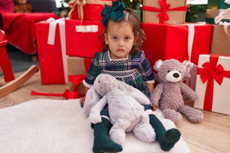 Photo for Adorable blonde toddler sitting on floor by christmas gifts with relaxed expression at home - Royalty Free Image