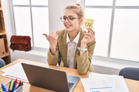 Photo for Young caucasian woman at the office calculating taxes pointing thumb up to the side smiling happy with open mouth - Royalty Free Image