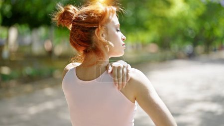 Photo for Young redhead woman wearing sportswear touching shoulder at park - Royalty Free Image