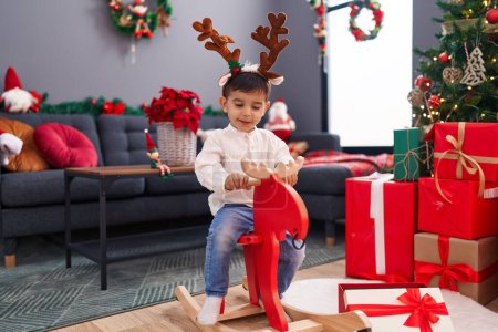 Foto de Adorable niño hispano jugando con renos meciéndose en el árbol de Navidad en casa - Imagen libre de derechos
