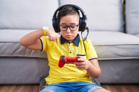 Photo for Young hispanic kid playing video game holding controller wearing headphones pointing down looking sad and upset, indicating direction with fingers, unhappy and depressed. - Royalty Free Image