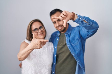 Téléchargez les photos : Mère hispanique et fils debout ensemble souriant faisant cadre avec les mains et les doigts avec le visage heureux. concept de créativité et photographie. - en image libre de droit