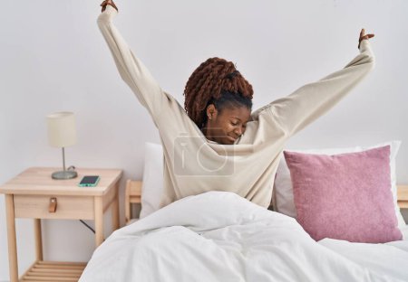 Téléchargez les photos : Femme afro-américaine se réveillant bras tendus dans la chambre - en image libre de droit