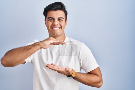 Photo for Hispanic man standing over blue background gesturing with hands showing big and large size sign, measure symbol. smiling looking at the camera. measuring concept. - Royalty Free Image