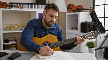 Photo for Young hispanic man musician composing song playing classical guitar at music studio - Royalty Free Image