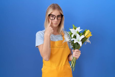 Photo for Young caucasian woman wearing florist apron holding flowers pointing to the eye watching you gesture, suspicious expression - Royalty Free Image
