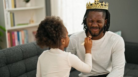 Foto de Padre e hija afroamericanos con corona de rey jugando con maquillaje en casa - Imagen libre de derechos