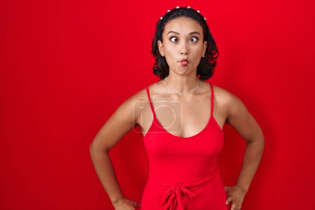 Photo for Young hispanic woman standing over red background making fish face with lips, crazy and comical gesture. funny expression. - Royalty Free Image