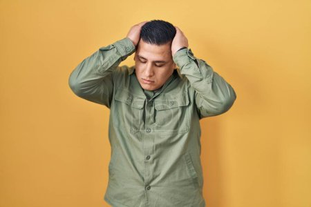 Photo for Hispanic young man standing over yellow background suffering from headache desperate and stressed because pain and migraine. hands on head. - Royalty Free Image