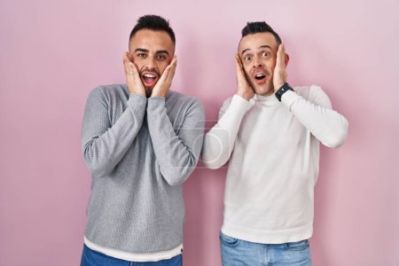 Photo for Homosexual couple standing over pink background afraid and shocked, surprise and amazed expression with hands on face - Royalty Free Image