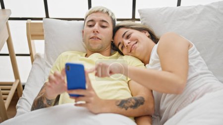 Téléchargez les photos : Beau couple utilisant smartphone couché sur le lit dans la chambre - en image libre de droit