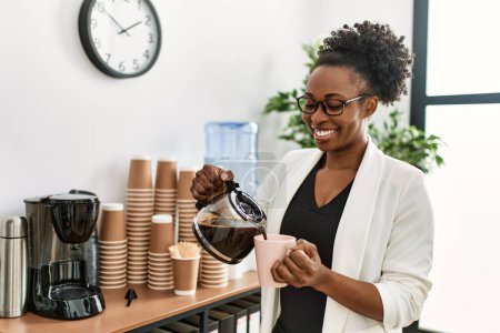 Téléchargez les photos : Femme afro-américaine ouvrière versant du café sur la tasse au bureau - en image libre de droit