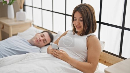 Téléchargez les photos : Beau couple couché sur le lit en utilisant un smartphone pendant que le petit ami dort dans la chambre - en image libre de droit