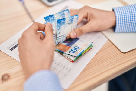 Téléchargez les photos : Jeune homme caucasien comptant les billets en francs suisses au bureau - en image libre de droit