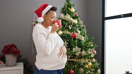 Photo for Young pregnant woman celebrating christmas smelling cup of coffee at home - Royalty Free Image