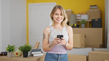 Téléchargez les photos : Jeune femme blonde utilisant smartphone debout à la nouvelle maison - en image libre de droit