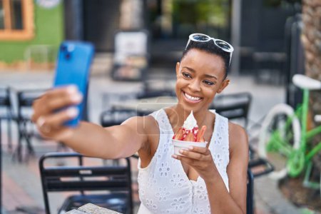 Photo for African american woman eating ice cream make selfie by smartphone at coffee shop terrace - Royalty Free Image