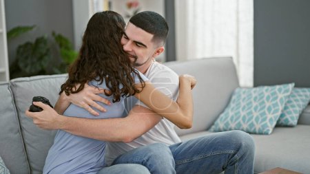 Photo for Smiling beautiful couple enjoying a winning video game at home, hugging each other in celebration indoors on their comfortable sofa - Royalty Free Image