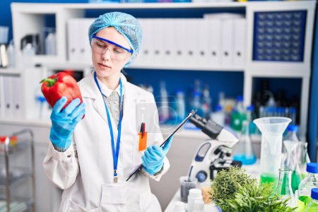 Foto de Joven rubia científica sosteniendo pimienta y lista de verificación en el laboratorio - Imagen libre de derechos