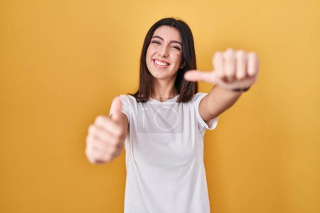 Photo for Young beautiful woman standing over yellow background approving doing positive gesture with hand, thumbs up smiling and happy for success. winner gesture. - Royalty Free Image