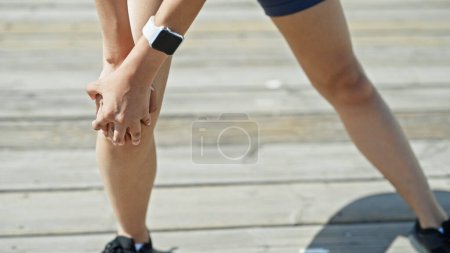 Foto de Joven mujer hispana hermosa usando ropa deportiva sufriendo por dolor de rodilla en la calle - Imagen libre de derechos