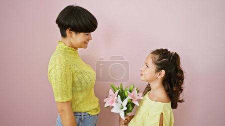 Téléchargez les photos : Mère et fille confiantes, ensemble dans la joie, debout sur un fond rose isolé, tenant un joli bouquet de fleurs de printemps, partageant une expression de style de vie heureux, souriant d'amour - en image libre de droit