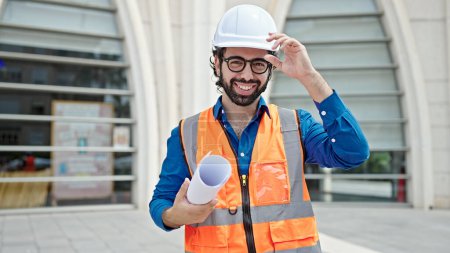 Photo for Young hispanic man architect smiling confident holding blueprints at construction place - Royalty Free Image