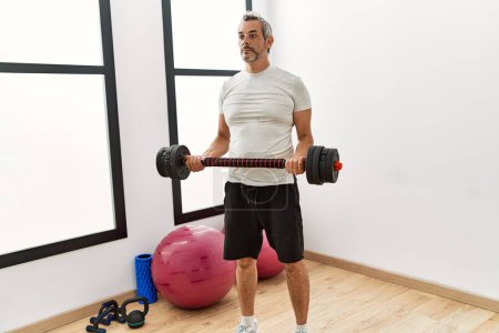 Photo for Middle age grey-haired man using weight training at sport center - Royalty Free Image