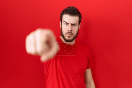 Téléchargez les photos : Jeune homme hispanique portant t-shirt rouge décontracté pointant mécontent et frustré à la caméra, en colère et furieux contre vous - en image libre de droit