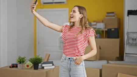 Foto de Mujer rubia joven hacer selfie por teléfono inteligente sonriendo en el nuevo hogar - Imagen libre de derechos