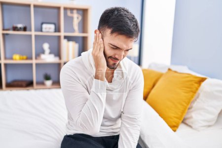 Photo for Young hispanic man suffering for ear pain sitting on bed at bedroom - Royalty Free Image