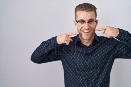 Téléchargez les photos : Jeune homme caucasien debout sur fond isolé souriant gai montrant et pointant avec les doigts dents et la bouche. concept de santé dentaire. - en image libre de droit