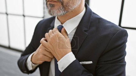 Foto de Atractivo, relajado, joven hispano, trabajador de negocios de cabello gris, concentrado, trabajando en su elegante lugar de trabajo interior. con corbata, chaqueta ejecutiva, en la oficina. - Imagen libre de derechos