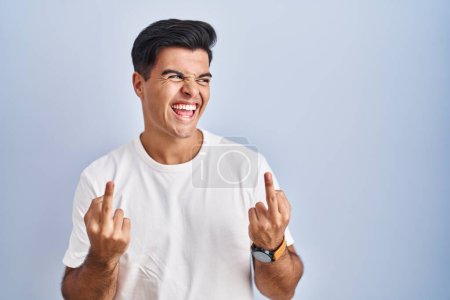 Foto de Hispanic man standing over blue background showing middle finger doing fuck you bad expression, provocation and rude attitude. screaming excited - Imagen libre de derechos