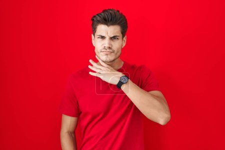 Téléchargez les photos : Jeune homme hispanique debout sur fond rouge couper la gorge avec la main comme couteau, menacer d'agression avec une violence furieuse - en image libre de droit