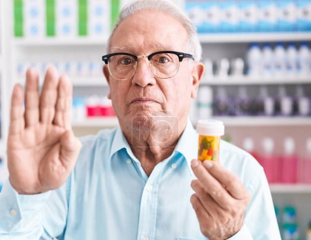 Photo for Senior man with grey hair holding pills at the pharmacy with open hand doing stop sign with serious and confident expression, defense gesture - Royalty Free Image