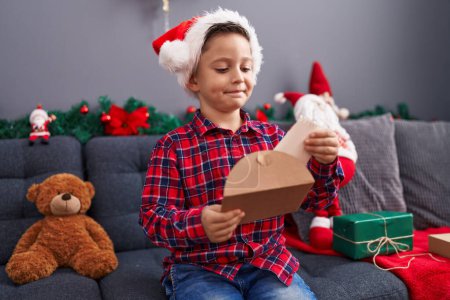 Foto de Adorable niño hispano poniendo carta de Santa Claus en sobre sentado por la decoración de Navidad en casa - Imagen libre de derechos