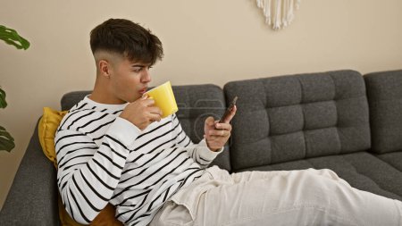 Photo for Young hispanic man using smartphone drinking coffee at home - Royalty Free Image