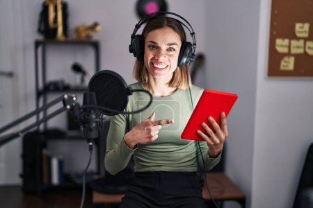 Téléchargez les photos : Femme hispanique chantant chanson en utilisant microphone et tablette souriant heureux pointant avec la main et le doigt - en image libre de droit